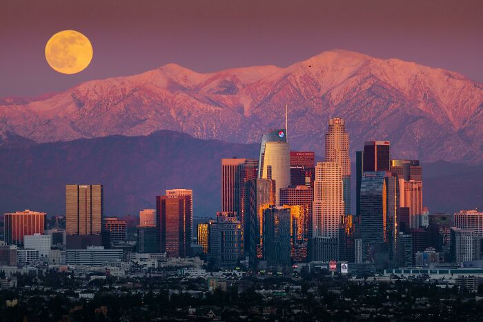 City skyline with snow-capped mountains and full moon at sunset, showcasing an amazing perspective of our world.