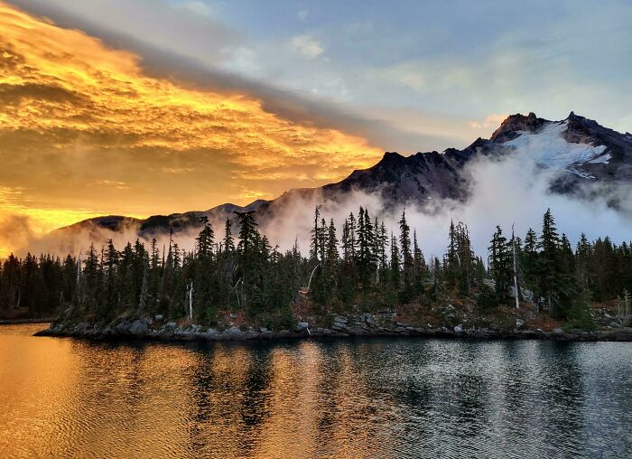 Sunset over a misty mountain and forest landscape reflected in calm water, showing our world from a different perspective.