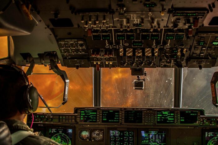 Pilot in a cockpit, surrounded by controls and screens, with a fiery sky outside, showcasing a different perspective of our world.