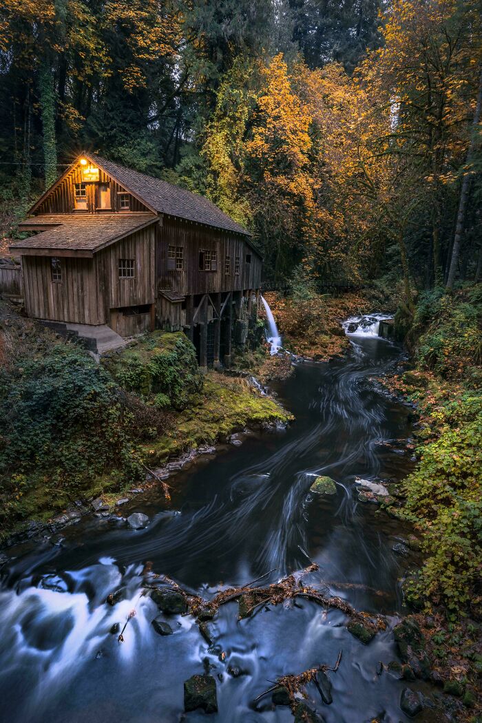 Rustic wooden mill beside a flowing river surrounded by autumn trees, showcasing our world from a different perspective.