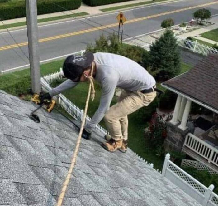 Man with zero common sense using a rope tied around his neck for safety while working on a steep roof.