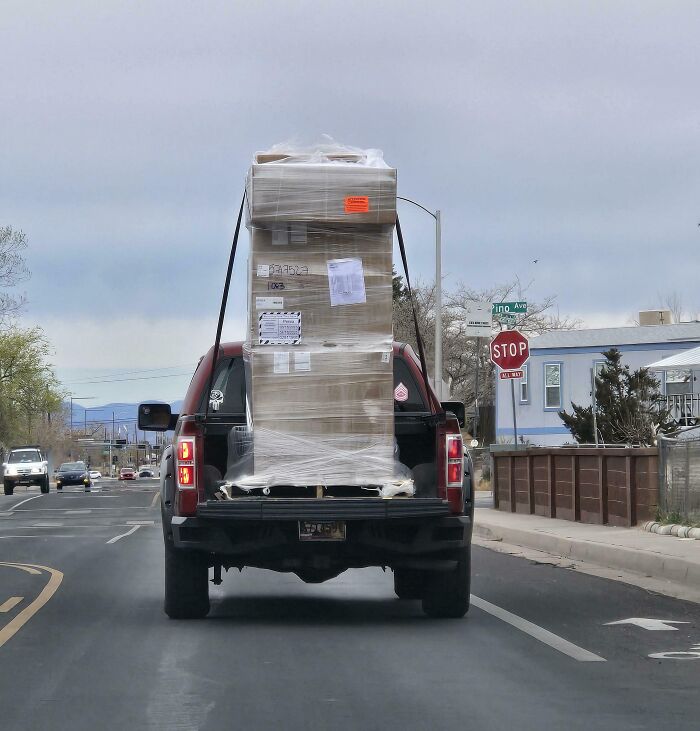 A large, unstable load strapped to the back of a pickup truck illustrating people with zero common sense.