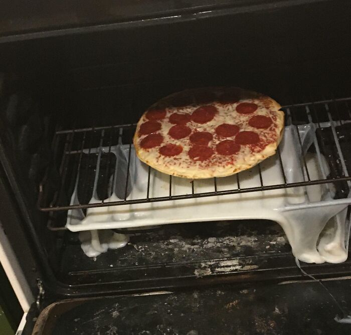 Frozen pepperoni pizza baking on oven rack above melting ceramic dishes, showcasing zero common sense cooking fail.
