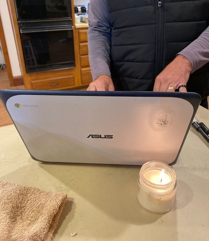 Person using ASUS Chromebook on kitchen counter near a lit candle, illustrating zero common sense situations.