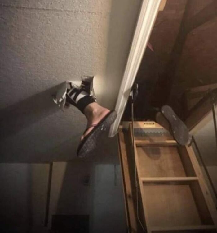 Person's legs stuck through ceiling hole next to attic ladder, showing lack of common sense in a home setting.