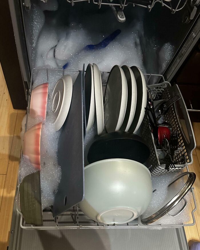 Dishwasher overflowing with soap suds and poorly loaded dishes, showing zero common sense in kitchen cleaning.