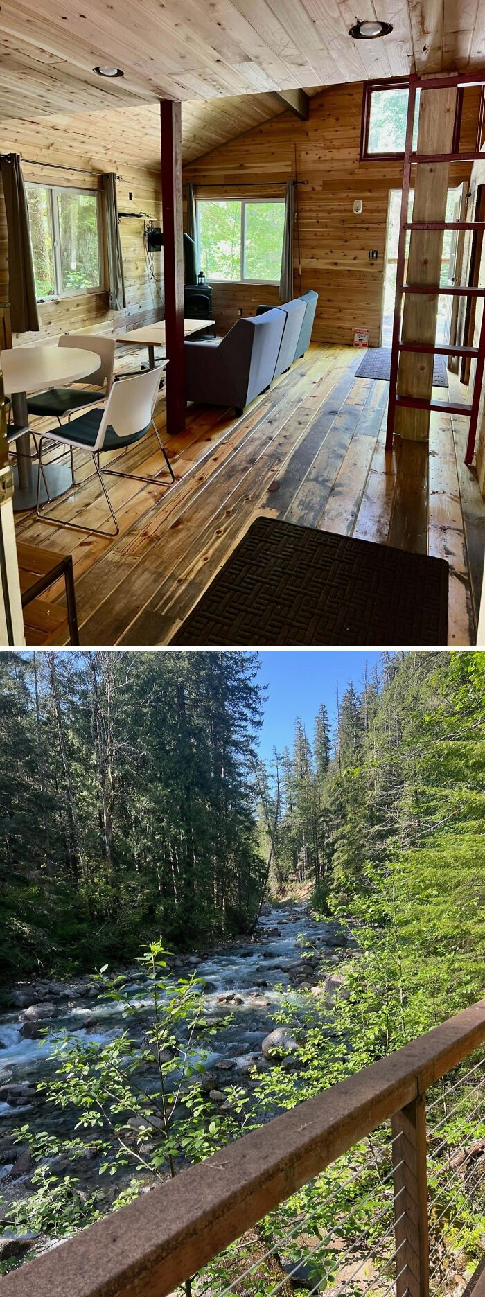 Cozy off-grid cabin interior with wooden walls and floors, overlooking a forested river view from the deck railing.
