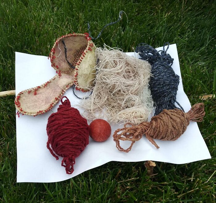 Baseball shown with its inside materials including yarn, leather, and cork laid out on a white sheet on grass in clear detail.