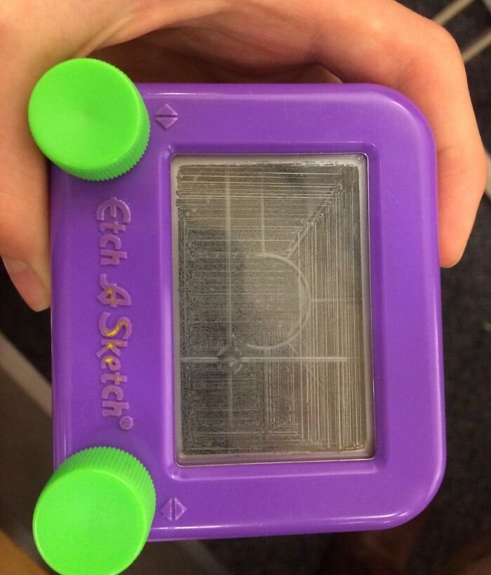 Close-up of the inside mechanism of a purple Etch A Sketch showing detailed internal lines and knobs.