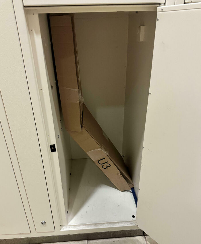 Cardboard box awkwardly stuck inside a small cabinet, illustrating a funny example of people not even trying at their job.