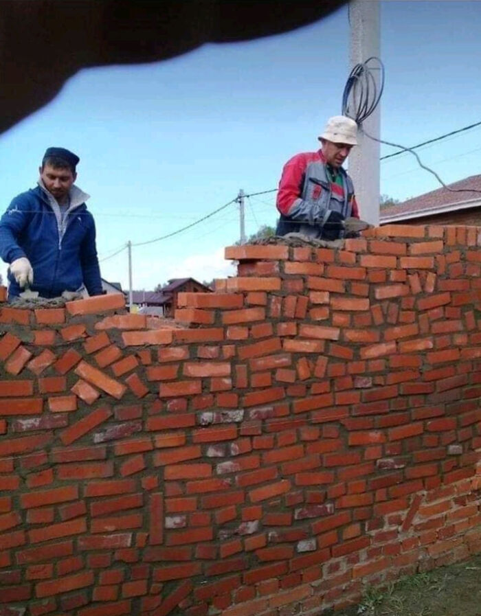 Two construction workers building a poorly aligned brick wall, showcasing funny examples of people not even trying.
