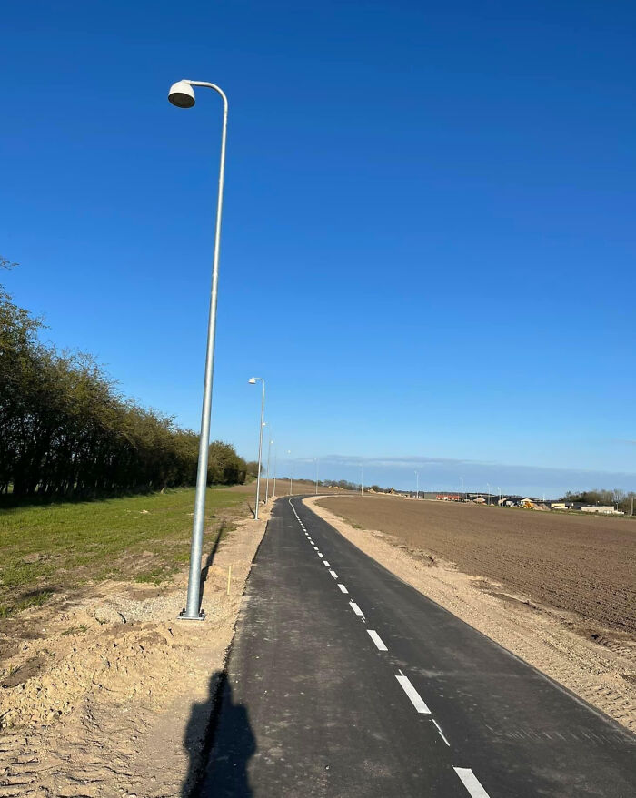 Street lamps installed alongside a paved road but only the first lamp has a bulb, showing people not even trying to finish the job.