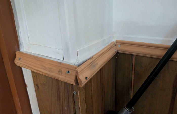 Poorly installed wood trim corner with visible screws and misaligned edges, a funny example of people not even trying at their job.