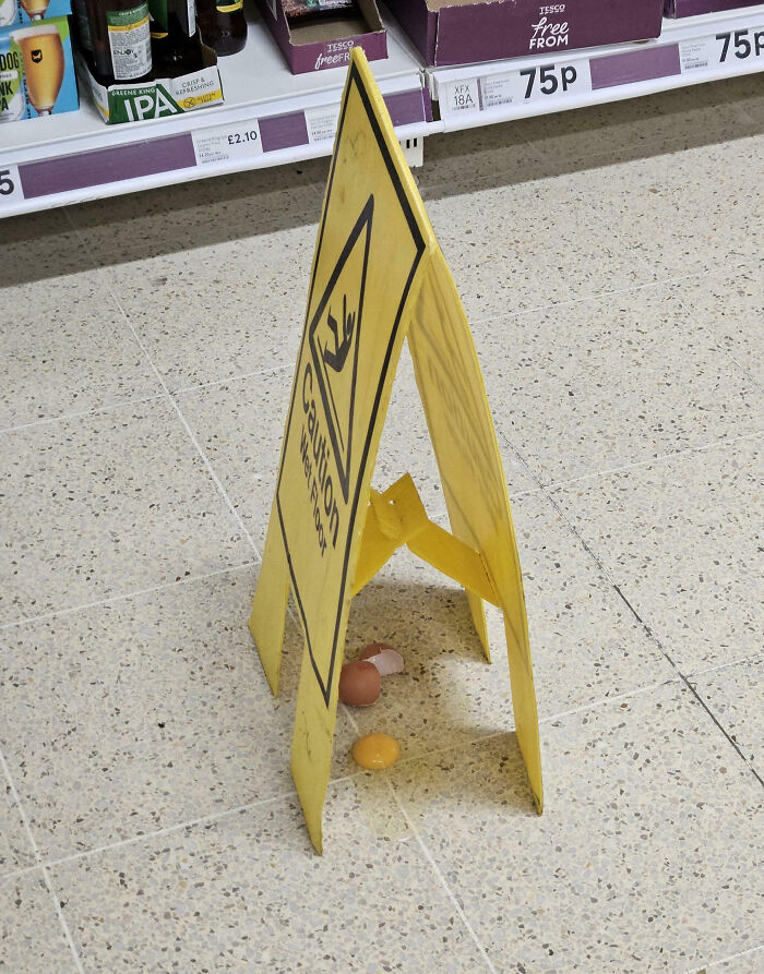 Yellow caution wet floor sign placed over broken eggs on supermarket floor, showcasing funny people not even trying moments.