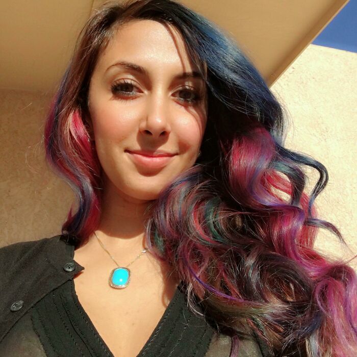 Young woman with vibrant multicolored hair smiling in natural light, showcasing creative dreams turned into reality and inspiring confidence.