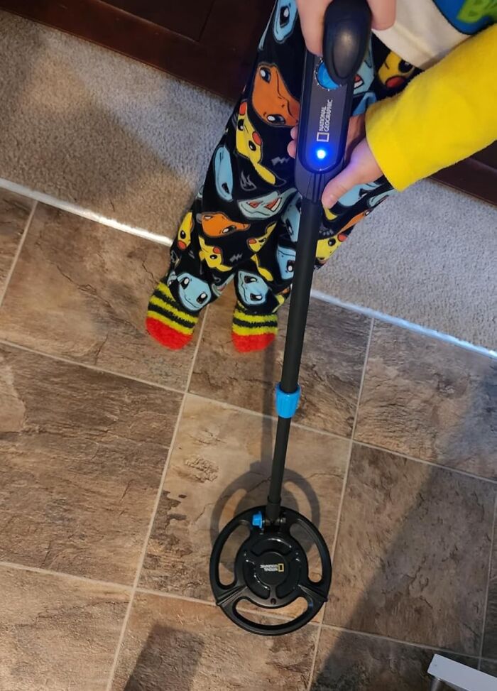 Child holding a metal detector on tiled floor wearing colorful character pajama pants and striped socks gift idea