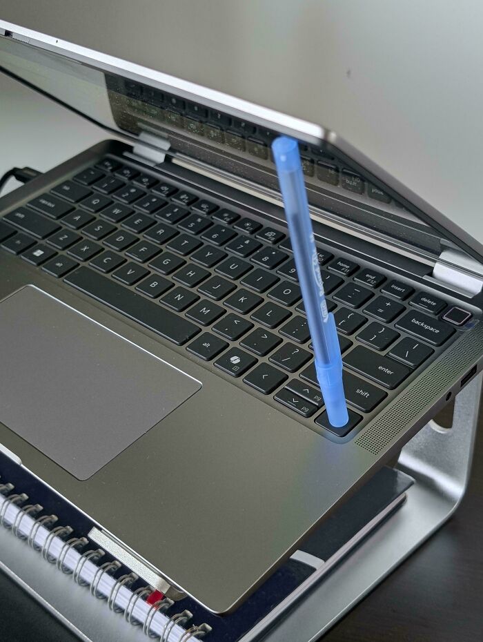 Blue pen held upright in a laptop keyboard slot, demonstrating one of the smart ideas and inventions that solve problems.