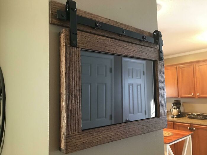 Wall-mounted smart mirror with rustic wooden frame and sliding hardware in a modern kitchen setting, showcasing smart ideas and inventions.