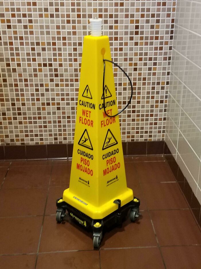 Yellow caution wet floor sign on wheels in a tiled room demonstrating smart ideas and inventions solving safety problems.