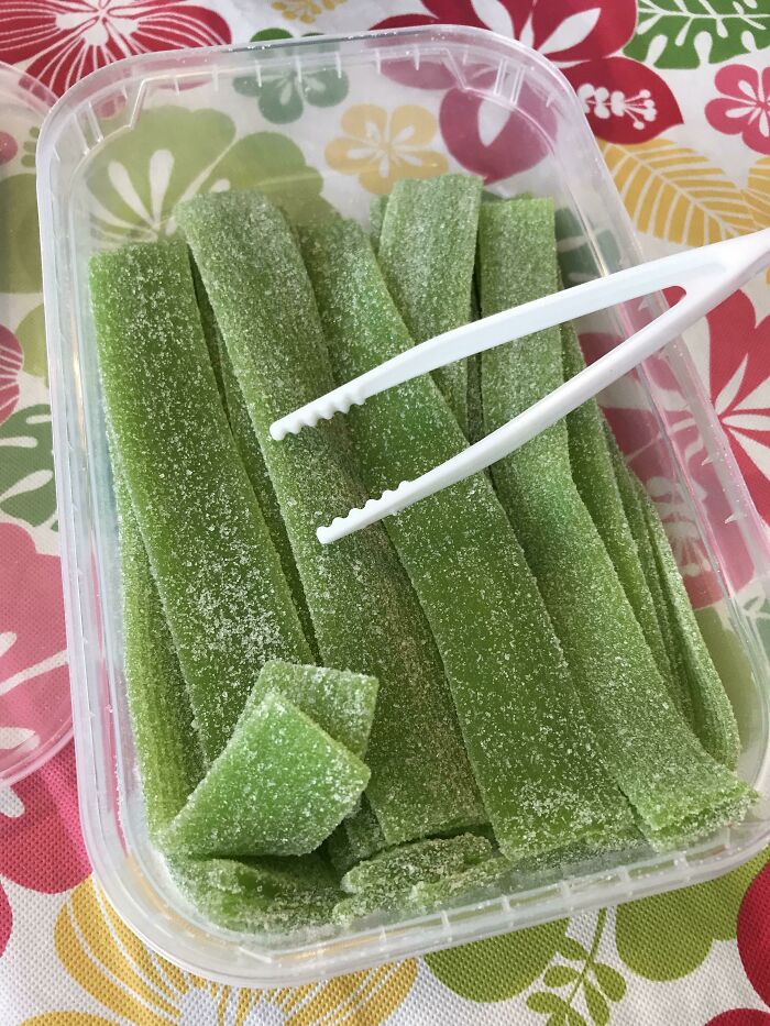 Green sour candy strips in a plastic container with white tongs on a colorful floral tablecloth, smart invention idea