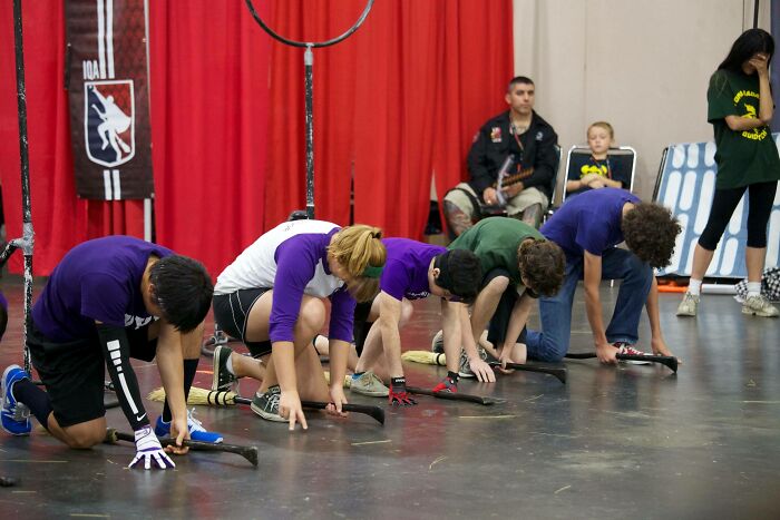 Group of young people preparing to race in a quidditch game indoors, captured with an epic photobomb stealing the show.