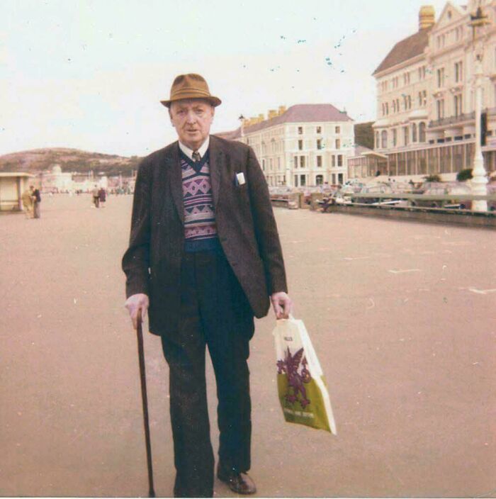 Elderly man with cane and shopping bag walking along a seaside promenade in a vintage where was this taken post.