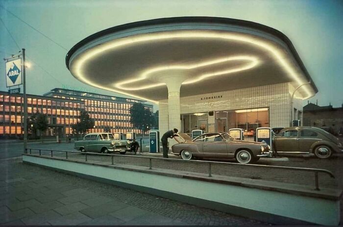 Vintage cars at a uniquely designed gas station with glowing circular roof, reflecting retro where was this taken internet posts theme.