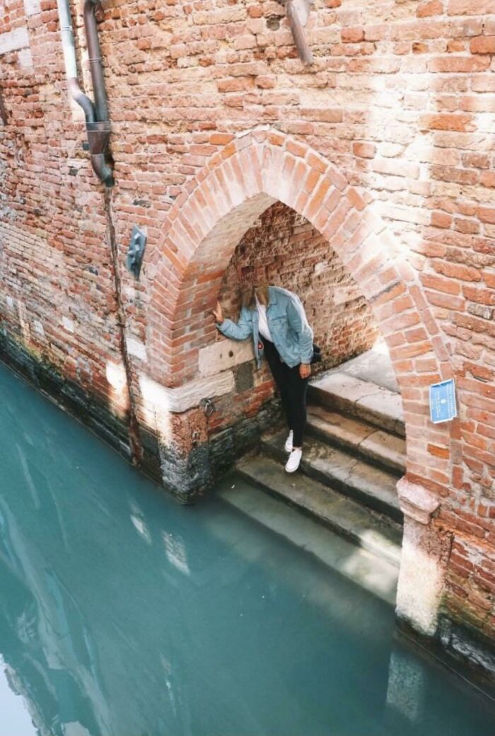 Person standing under a brick archway beside a narrow canal, illustrating intriguing where was this taken posts online.
