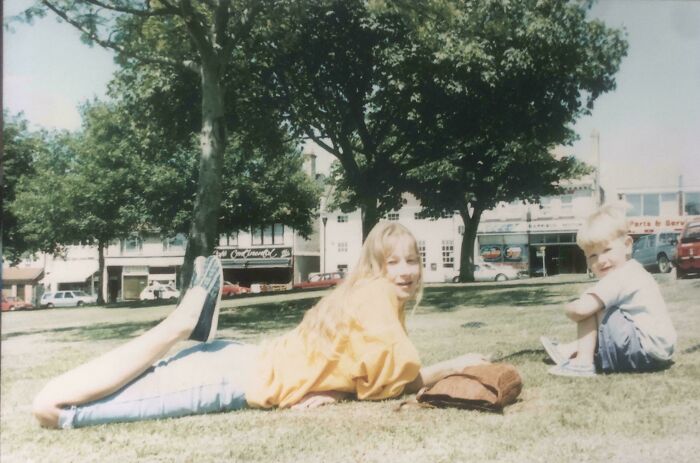 Two children relaxing on grass in a sunny park, perfect example for where was this taken internet posts.
