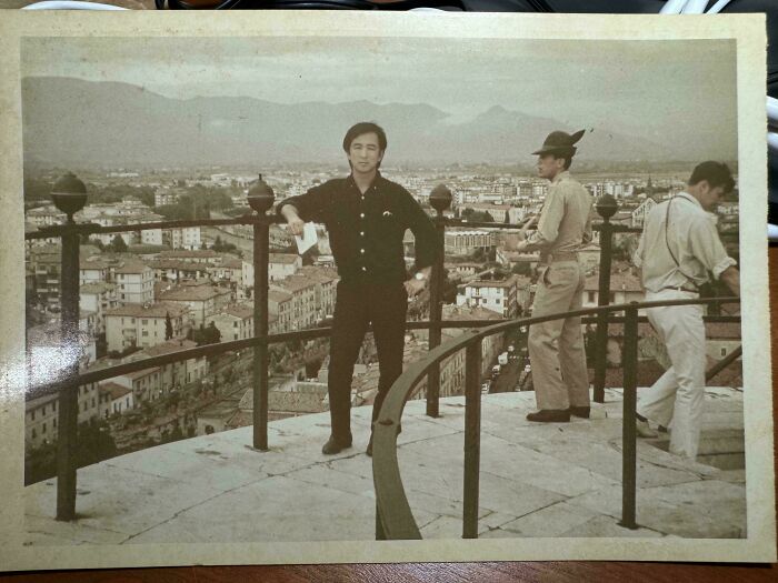Three men standing on an elevated viewpoint overlooking a cityscape with mountains in the background location unknown