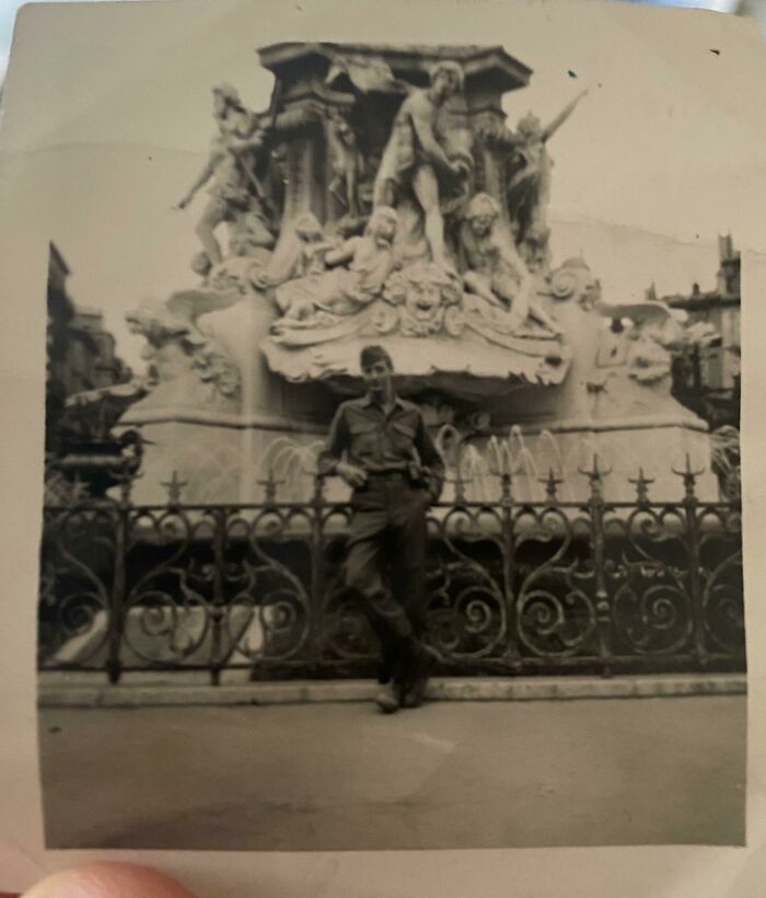 Black and white vintage photo of a man posing in front of a detailed stone sculpture with ornate railing, where was this taken.