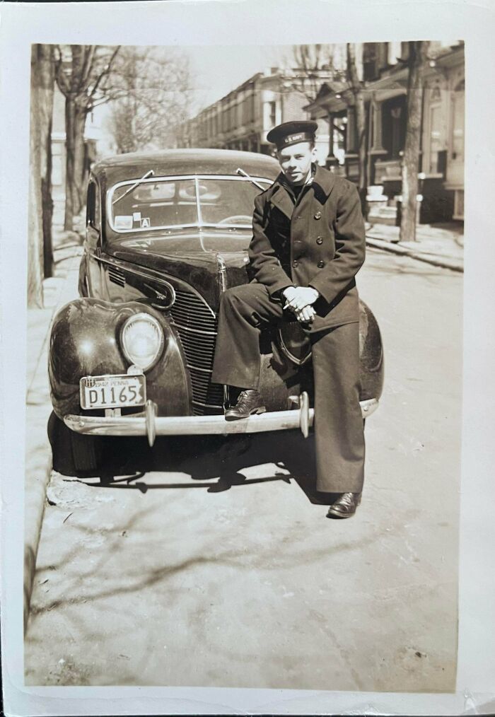 Vintage black and white photo of a US Navy sailor leaning on a classic car on a city street, where was this taken question.