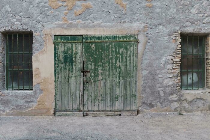 Old weathered green wooden door and two barred windows in a c*****d stone wall, creating a rustic scene for where was this taken posts.
