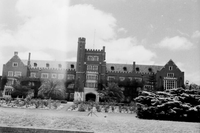 Black and white photo of a large historic building surrounded by gardens and trees where was this taken mystery post