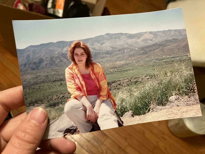 Hand holding a photo of a woman sitting outdoors with mountains in the background, a popular where was this taken post.