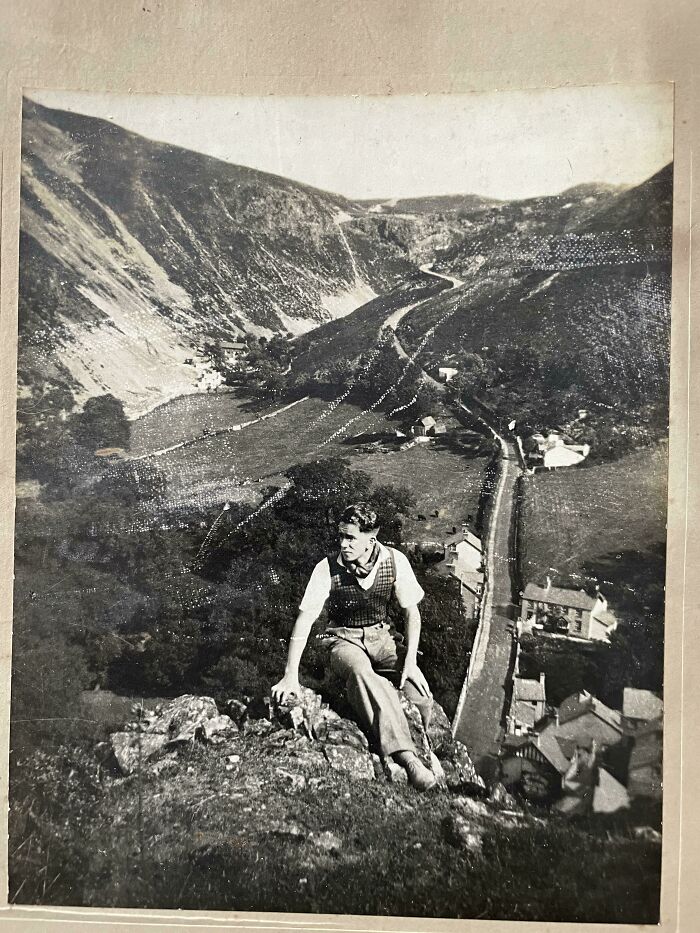 Vintage photo of a man sitting on a rock overlooking a valley and village, from where was this taken posts online.
