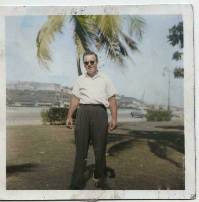 Vintage photo of a man standing outdoors under a palm tree, an example of popular where was this taken posts online.