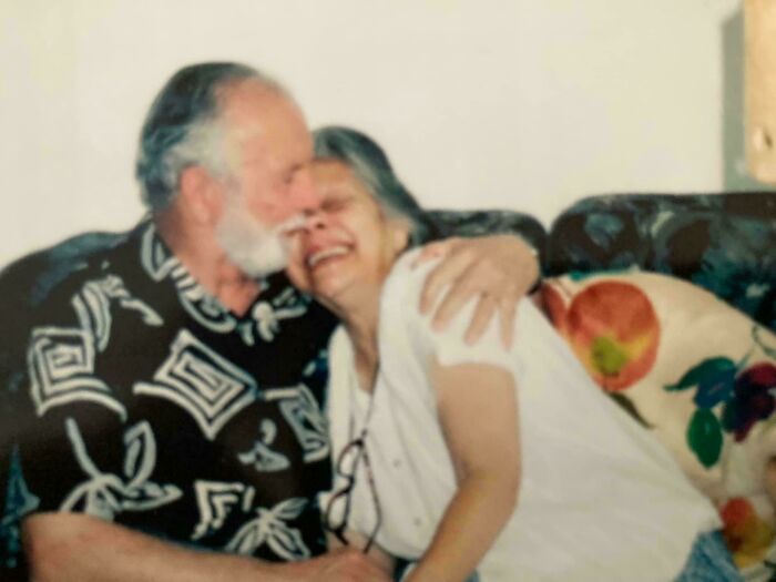 Elderly siblings sharing a joyful moment with a warm embrace on a couch, showing gratitude and love.
