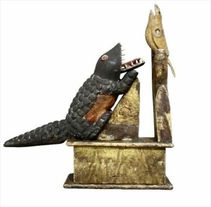 Ancient carved wooden alligator figure sitting on a box with gold and brown patina, showing very old objects from ancestors.