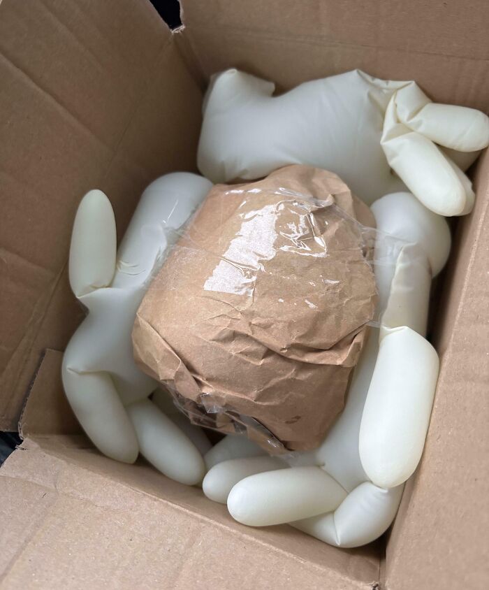 Inflated gloves used as smart packaging solution cushioning a taped brown paper-wrapped item in a cardboard box.