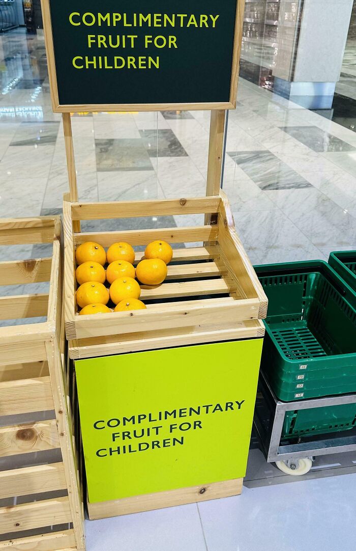 Wooden crate with complimentary fruit for children in a public space, showcasing a simple invention that solves a problem.