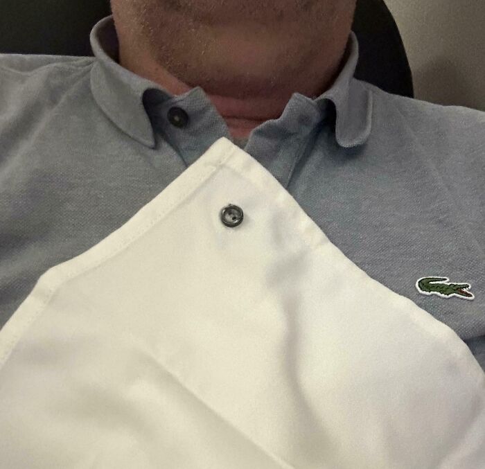 Man wearing a grey polo shirt with a white apron secured by a snap button shown in a close-up view.