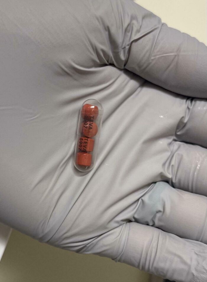 Gloved hand holding a clear capsule containing three small orange smart invention pills solving a medication problem