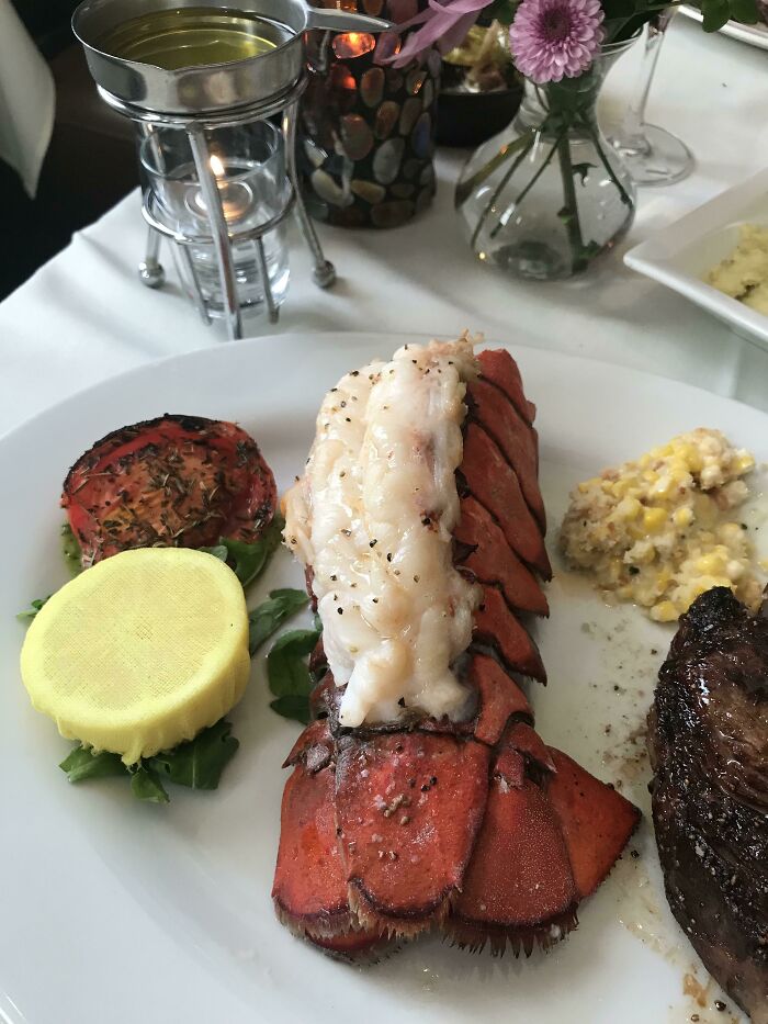 Lobster tail and steak plated with grilled tomato and creamed corn, highlighting juicy steak and buttery lobster dinner.
