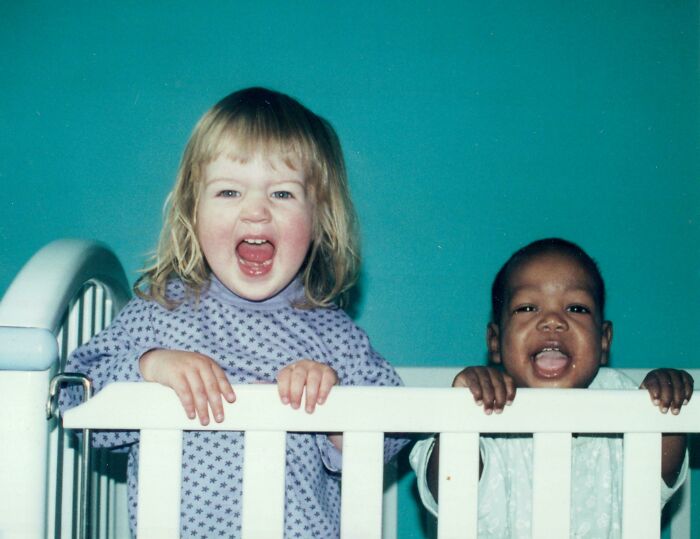 Two young siblings smiling and laughing together while standing in a white crib against a blue background