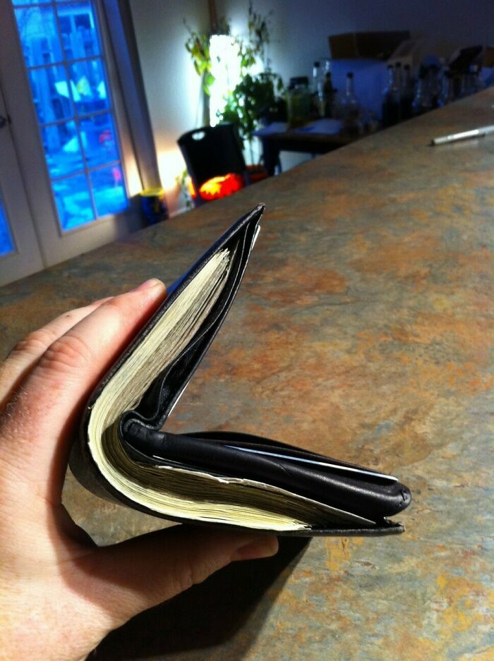 Hand holding a thick wallet full of cash on a kitchen counter, illustrating funny steak and lobster complaints.