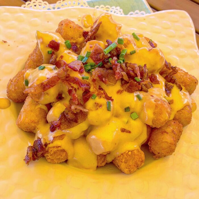 Plate of crispy tater tots topped with melted cheese, bacon bits, and chopped green onions, showcasing juicy and buttery flavors.