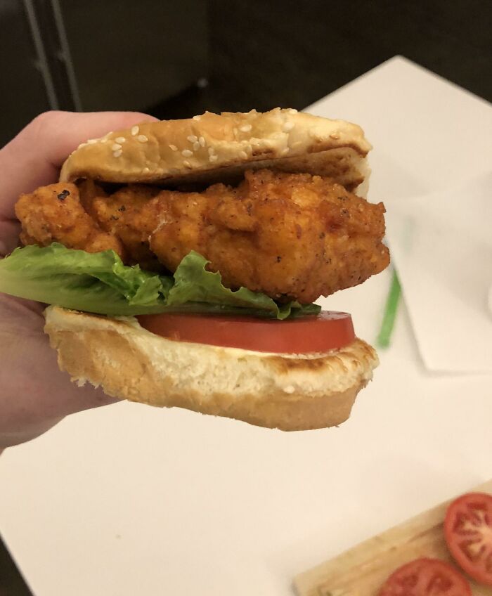 Hand holding a crispy fried chicken sandwich with lettuce and tomato, illustrating funny steak and lobster complaints.