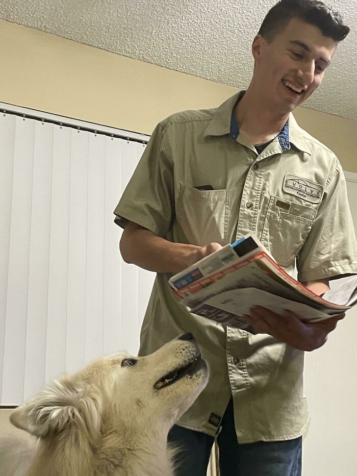 Man smiling while holding papers with a dog looking up, reflecting moments of big and small dreams turned into reality.