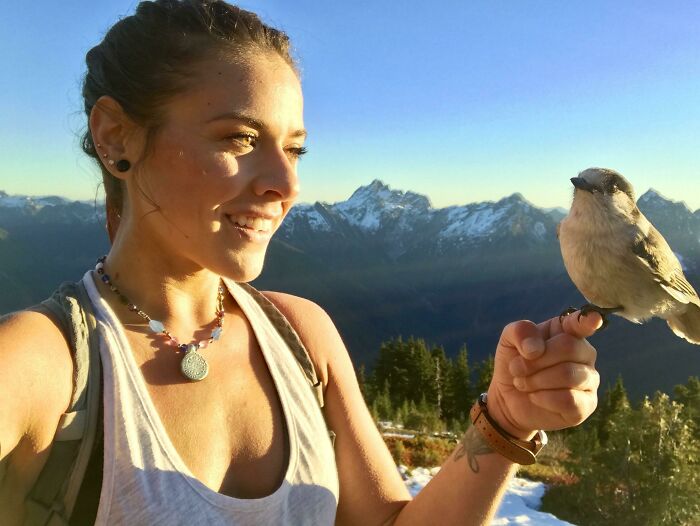 Woman in a mountain setting smiling while holding a small bird, capturing moments of dreams turned into reality.